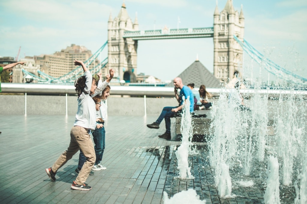 Kinder in London spielen an öffentlichem Wasserstrahl vor der Tower Bridge