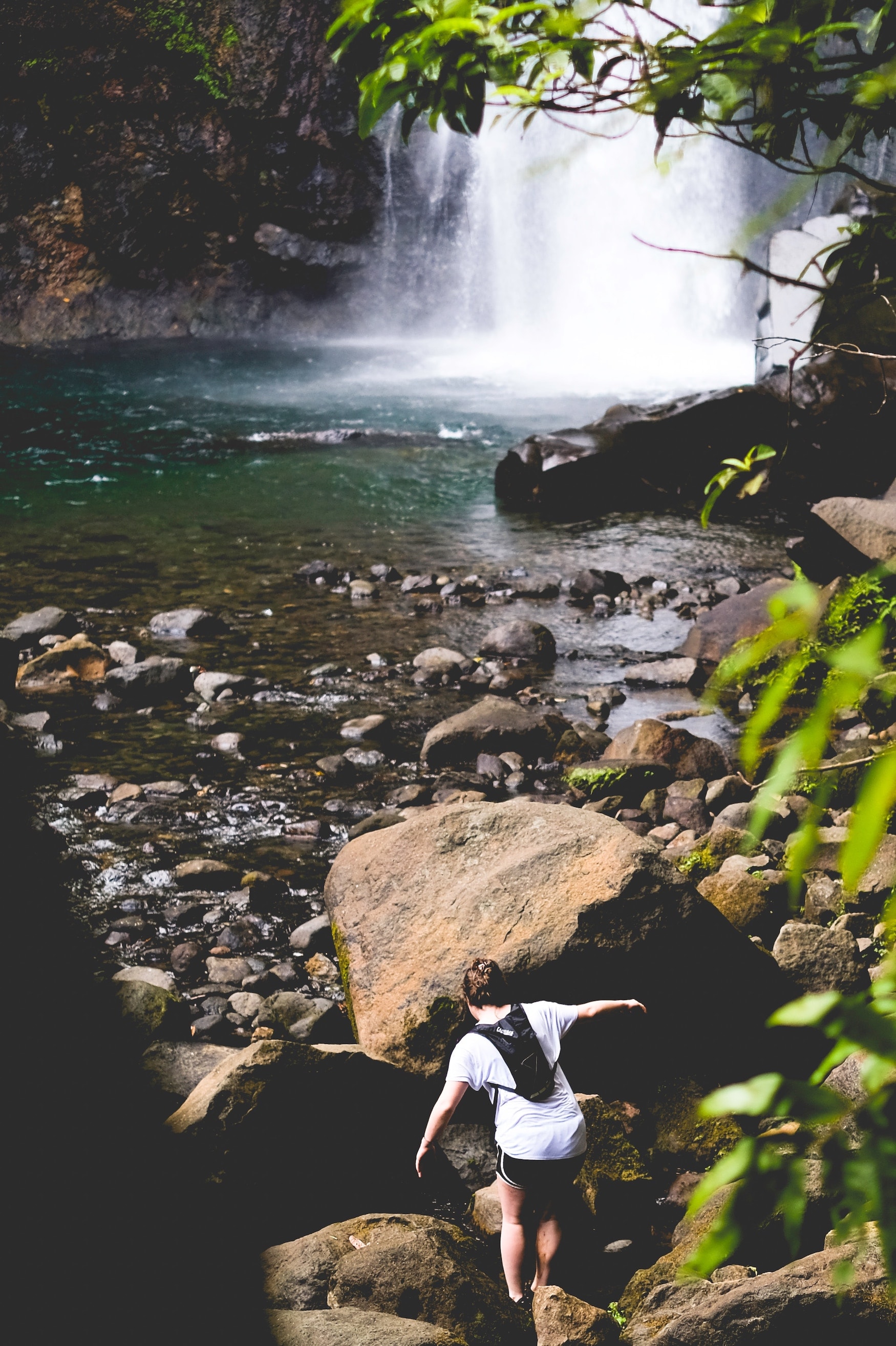 Frau klettert über Steine zu Wasserfall