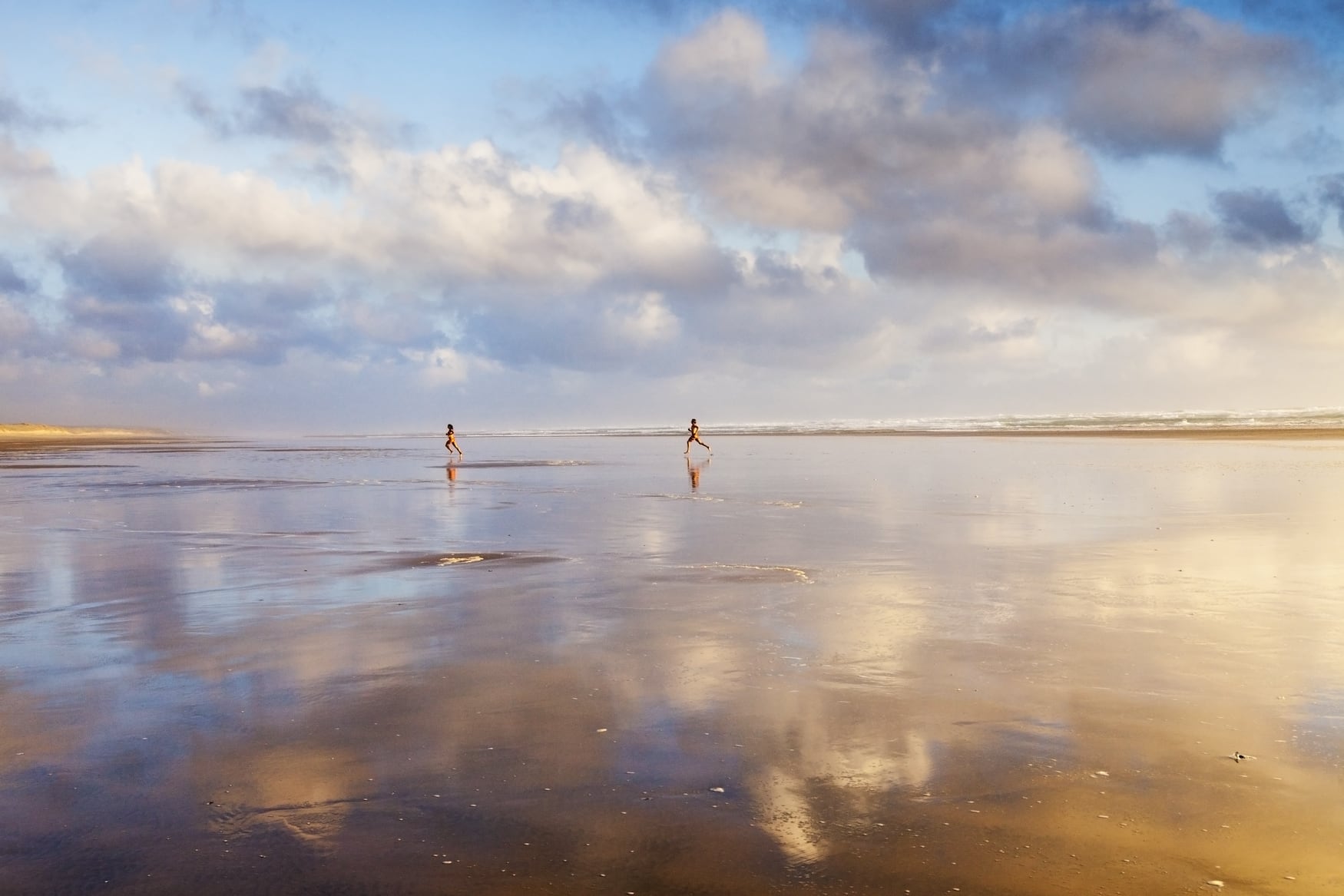 Zwei Frauen springen am Wasser entlang am Ninety Mile Beach in Neuseeland