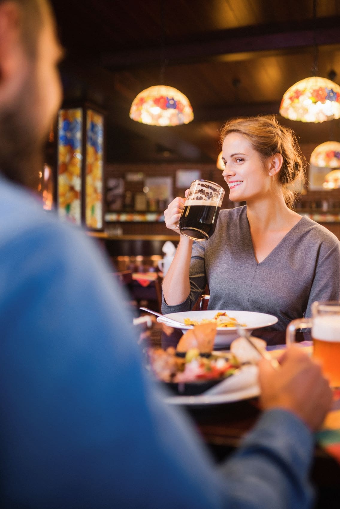 Frau an Tisch im Restaurant trinkt lächelnd ein Bier
