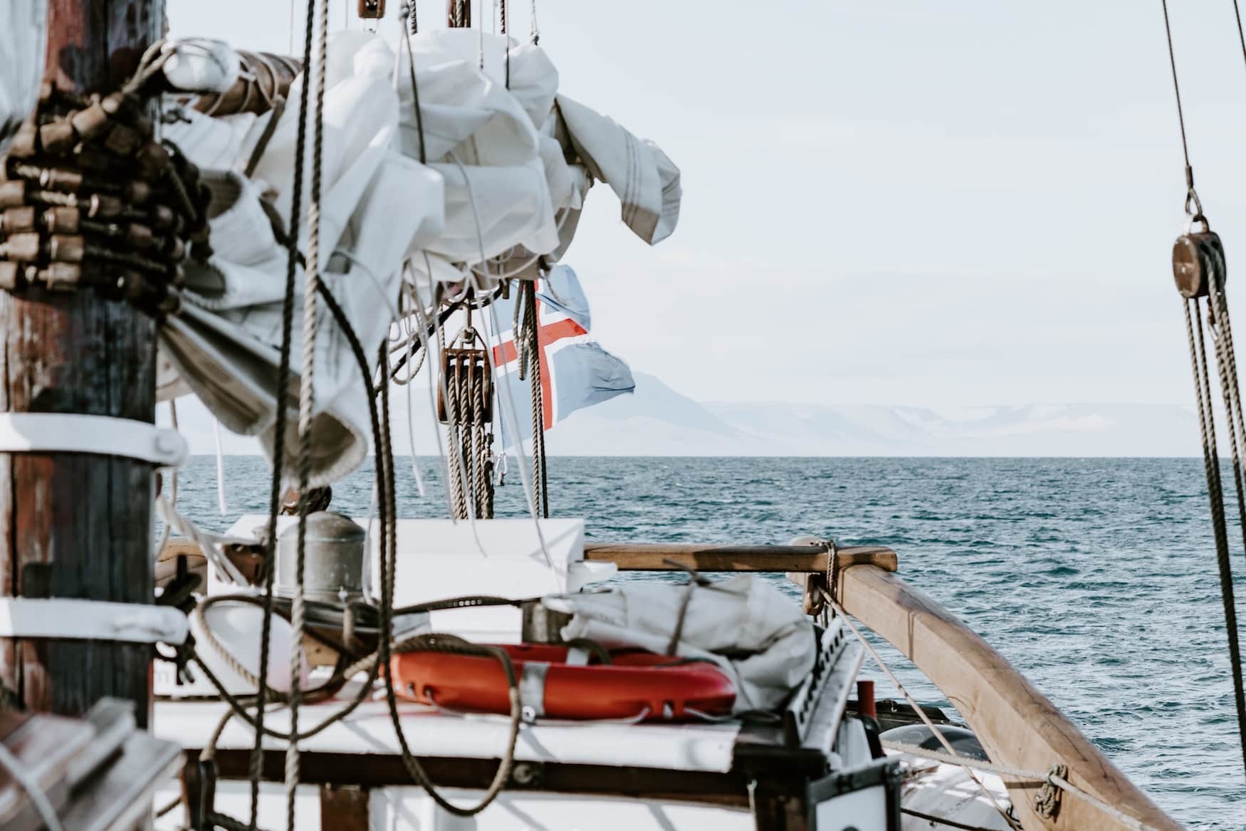 Segelschiff fährt auf offenem Gewässer. Grönland Flagge weht im Wind