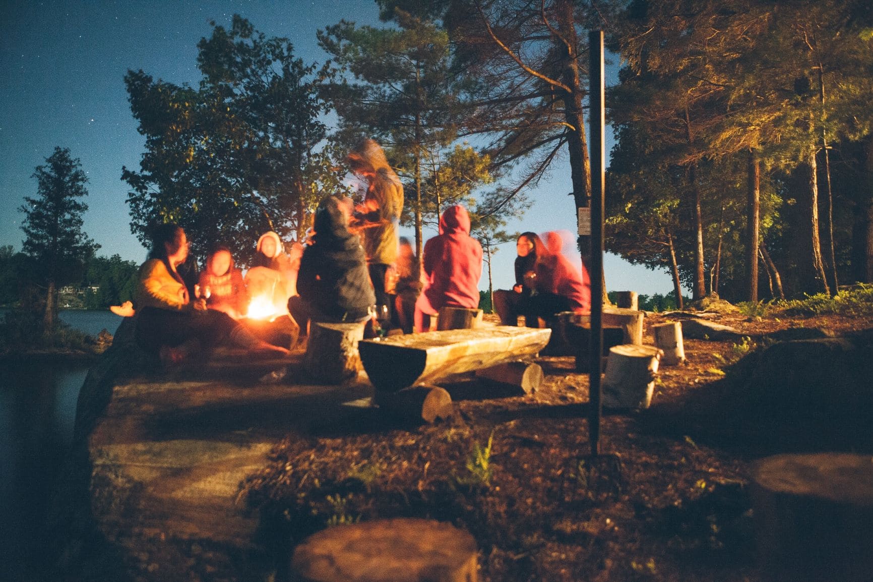 Besucher eines Campingplatzes sitzen abends im Kreis am Feuer