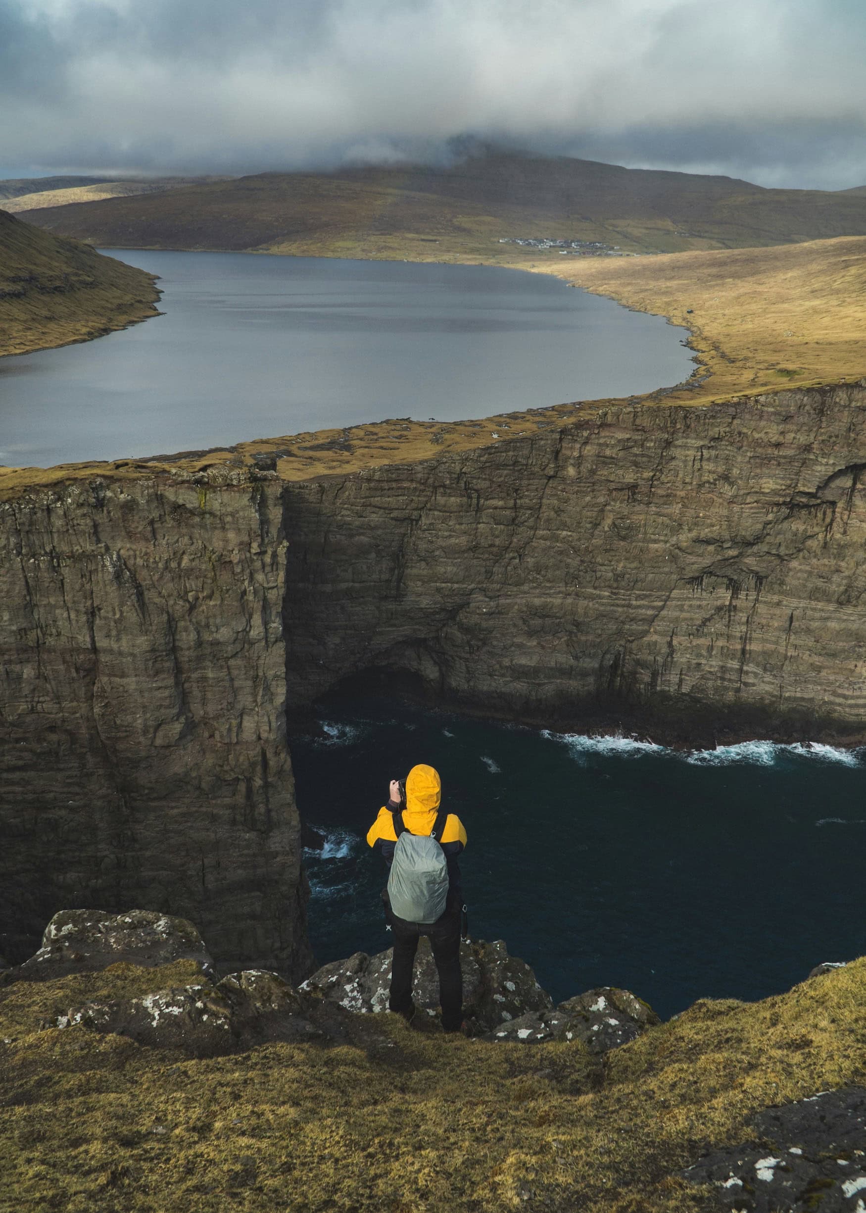 Wanderer steht am Kliffrand über dem Atlantik, dahinter der See Sørvágsvatn auf den Färöer-Inseln.