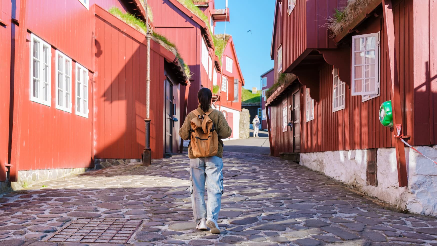 Spaziergängerin in der Altstadt von Tórshavn mit roten Holzhäusern und Grasdächern, Färöer-Inseln.
