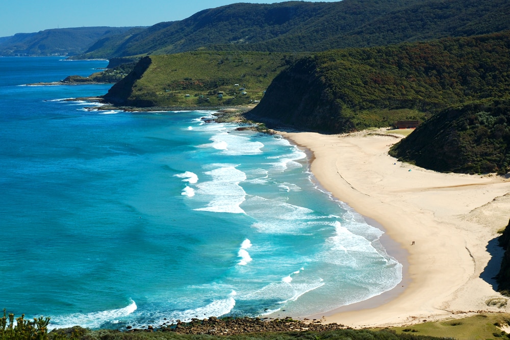 Weißer Strand an Ozean und bewachsenen Hügeln