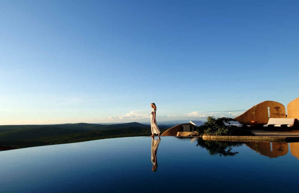 Frau spaziert über Infinity Pool vor Landschaftskulisse Kenias