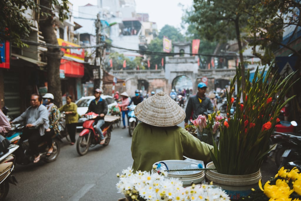 Frau mit Reishut schiebt ihr Fahrrad durch Straßen von Hanoi
