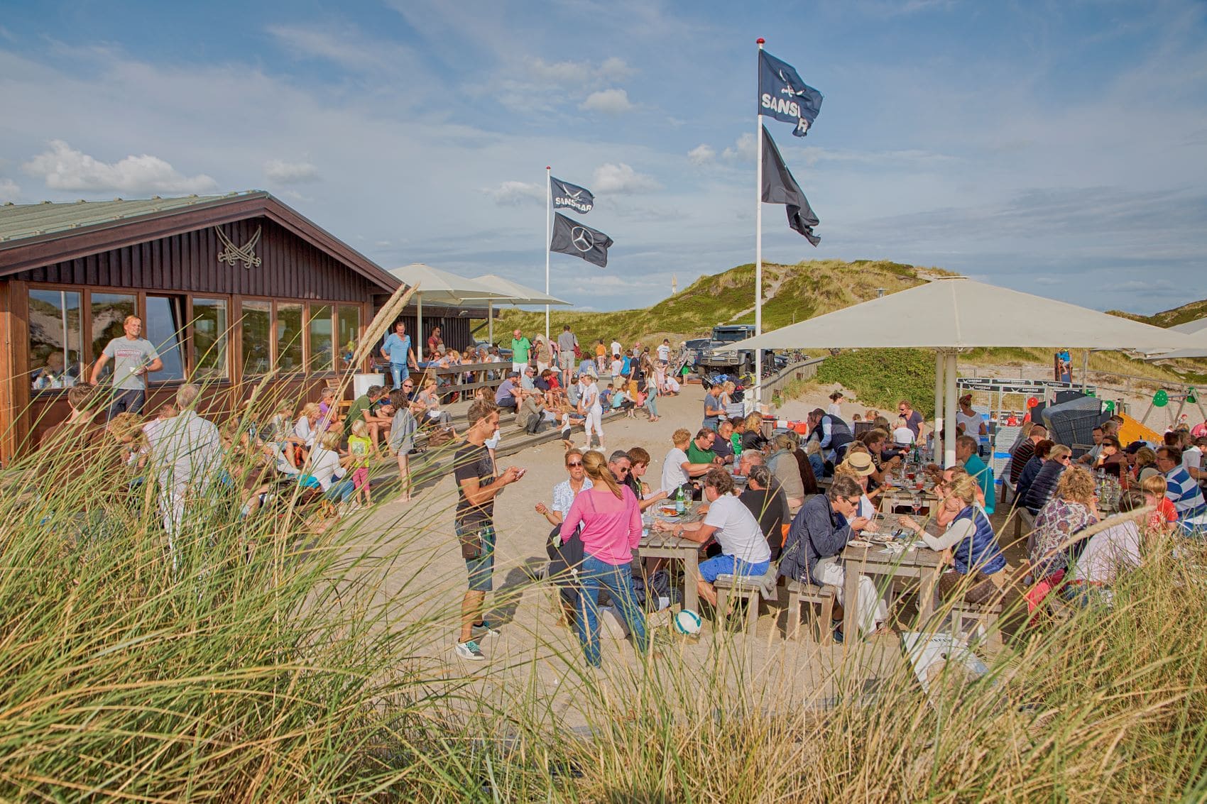 Gäste im Biergarten der Sansibar auf Sylt an einem windigen Sommertag