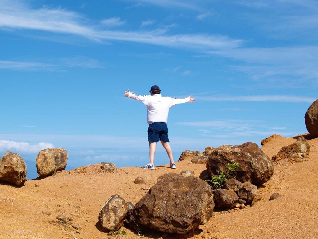 Steine am Strand und ein Mann der die Arme ausbreitet auf Lanai