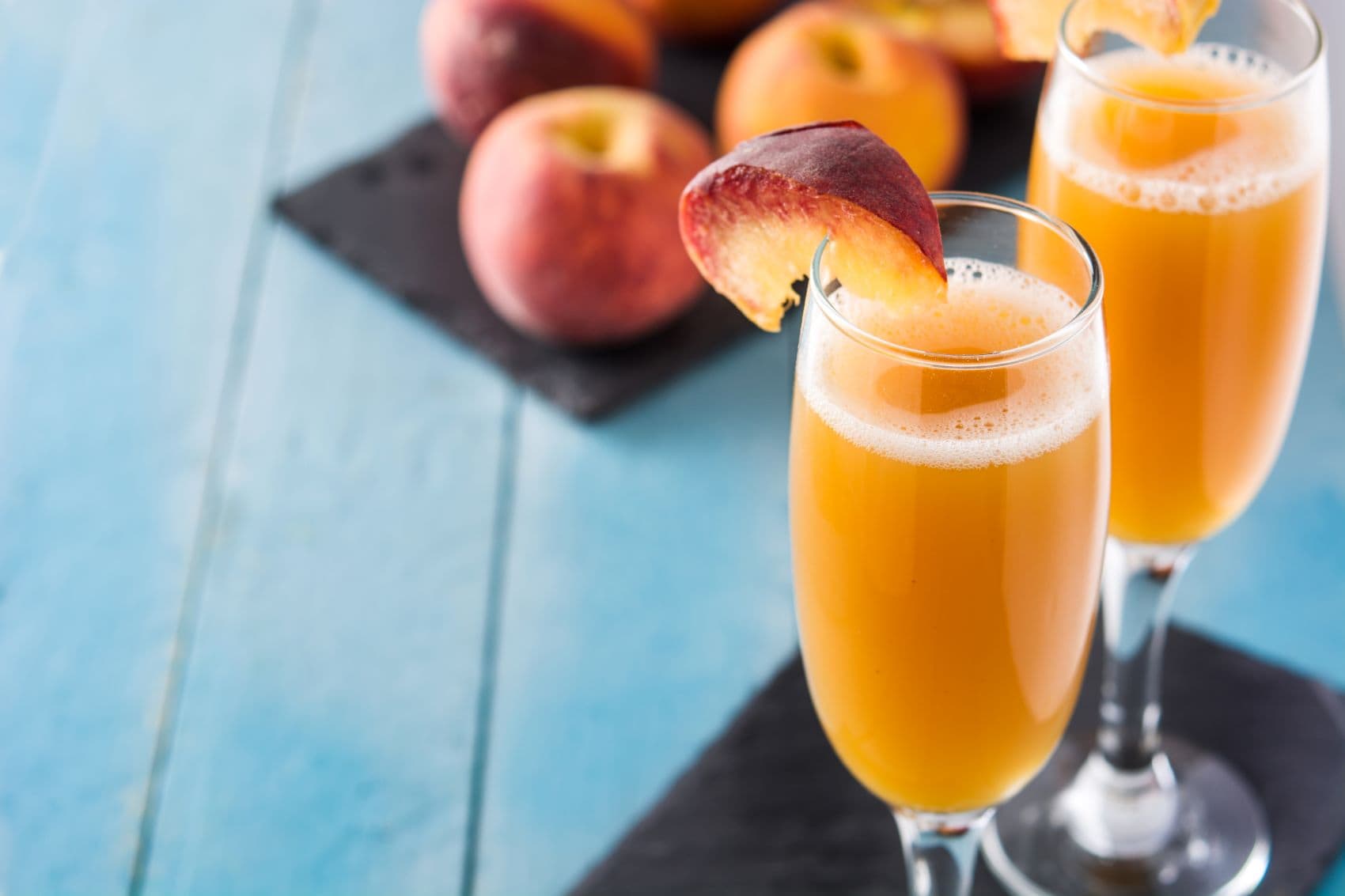 Zwei Bellini-Cocktails, im Hintergrund Pfirsiche 