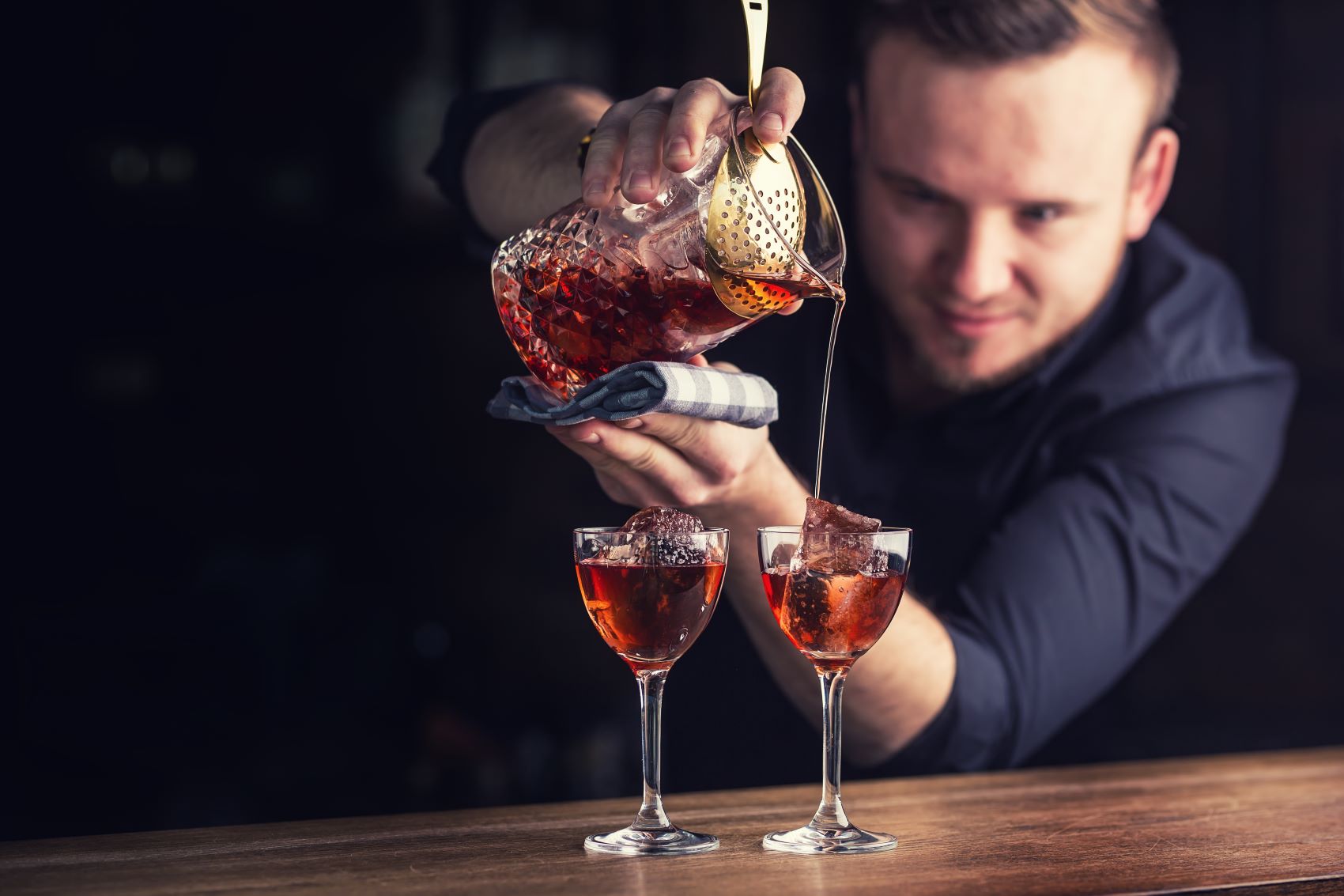 Barkeeper schüttet Manhatten-Cocktail in zwei Gläser 