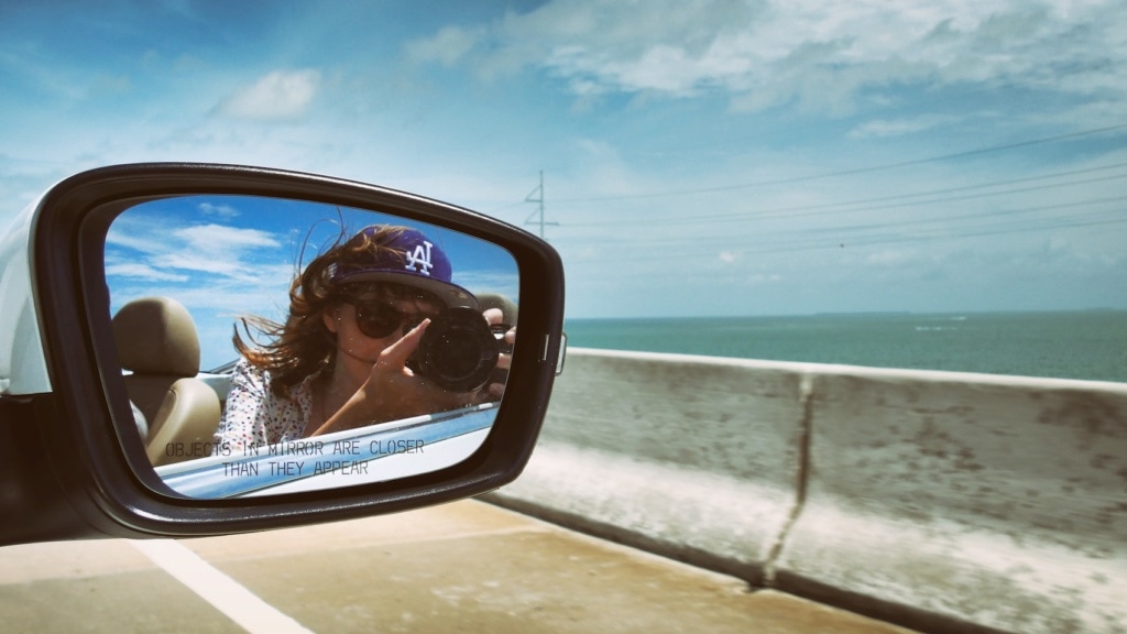 Frau im Rückspiegel mit kamera fährt in einem Cabrio über die Brücken der Florida Keys
