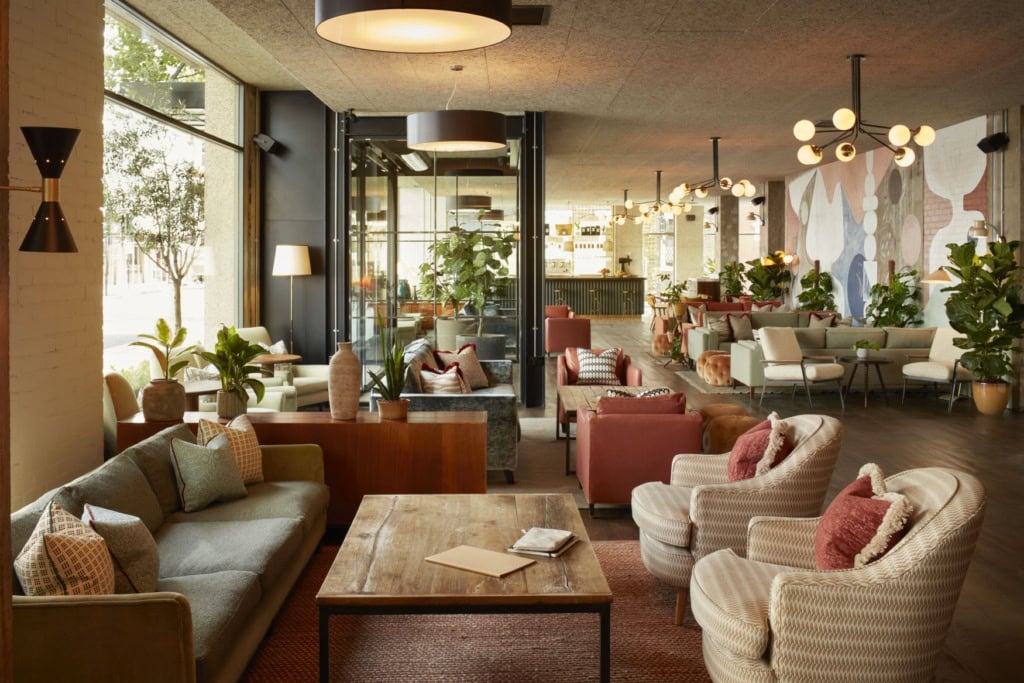 Blick in eine elegante Hotellobby mit Polstermöbeln in Pastellfarben und viel Sichtbeton.