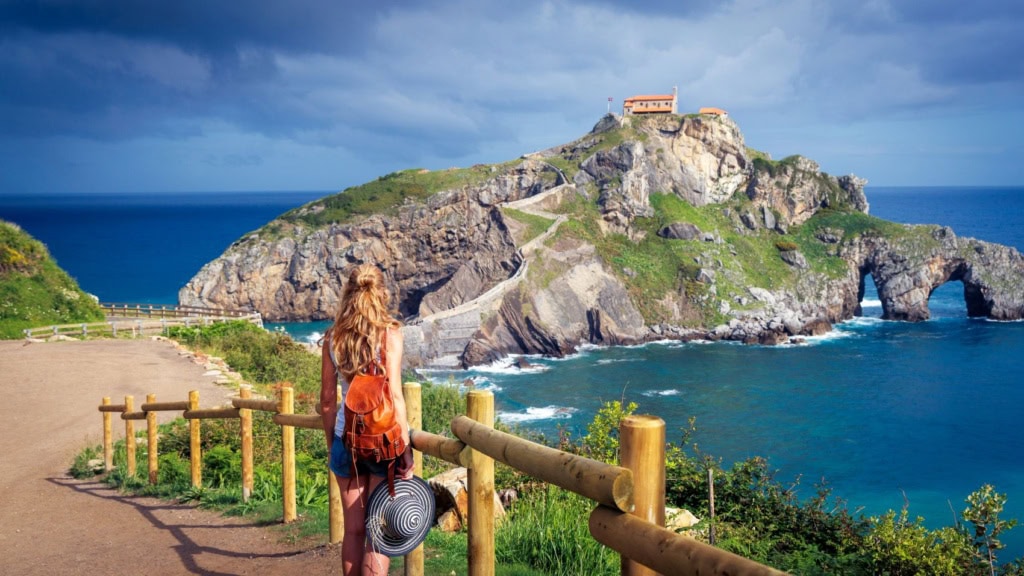 Junge Frau blickt auf San Juan de Gaztelugatxe im Baskenland, Spanien