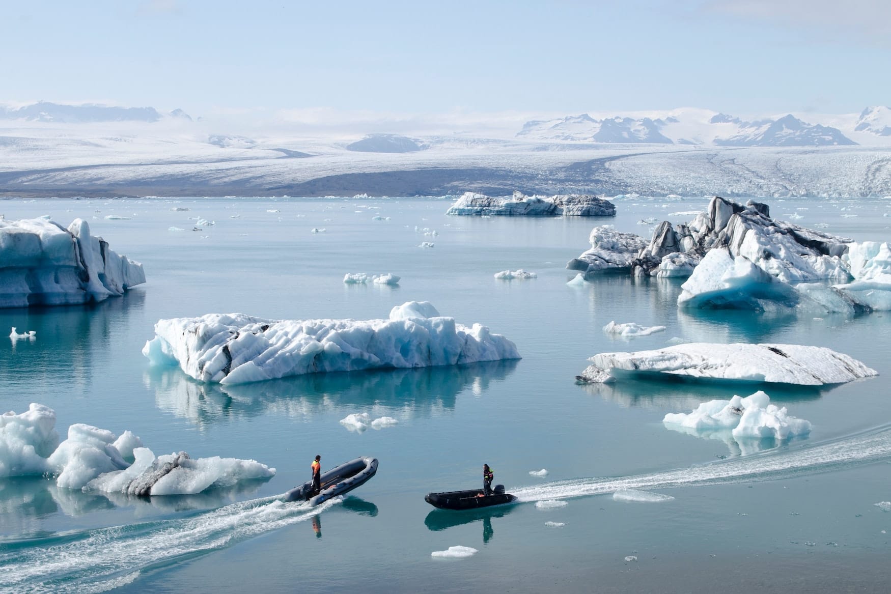 Kleine Boote fahren über See in Island. Überall liegen große Eisbrocken im Wasser.