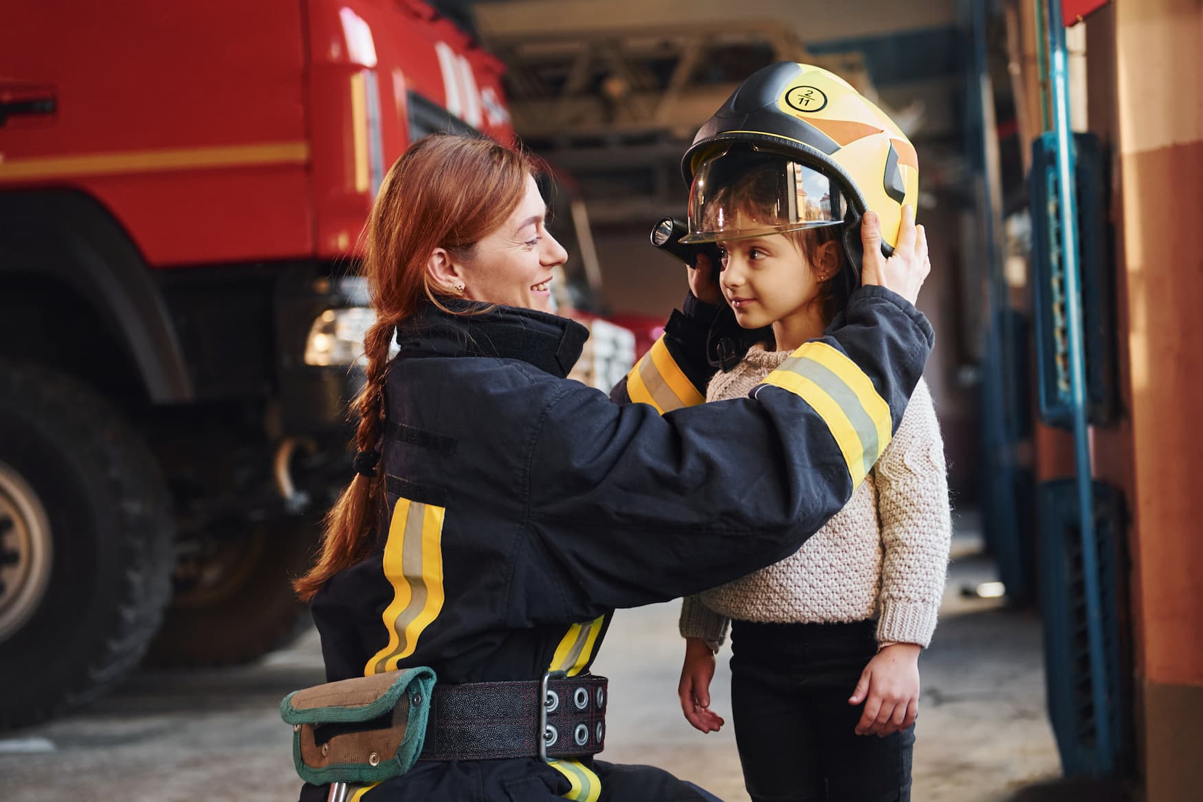 Kleines glückliches Mädchen kriegt Helm von Feuerwehrfrau aufgesetzt