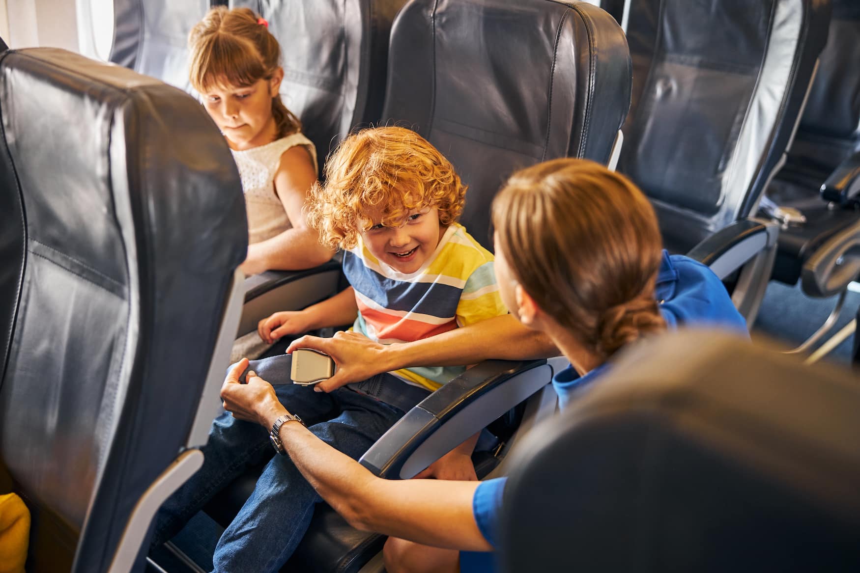 Zwei Alleinreisende Kinder werden von Flugbegleiterin im Flugzeug angeschnallt