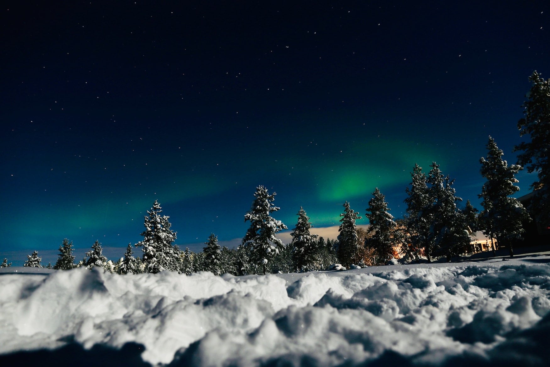 Schnee-Landschaft in Sodankylä, im Hintergrund sind grüne Nordlichter zu sehen