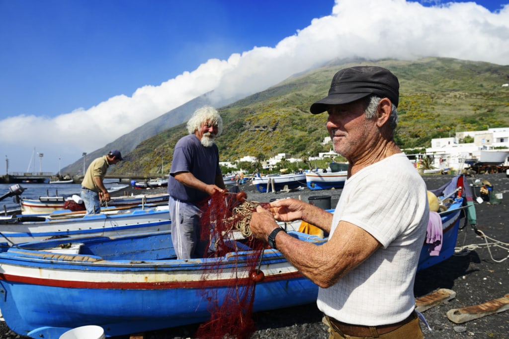 Fischer reparieren Netze am Scari-Strand, im Hintergrund der Vulkan, Insel Stromboli, Liparische oder Äolische Inseln, Sizilien, Italien, Europa