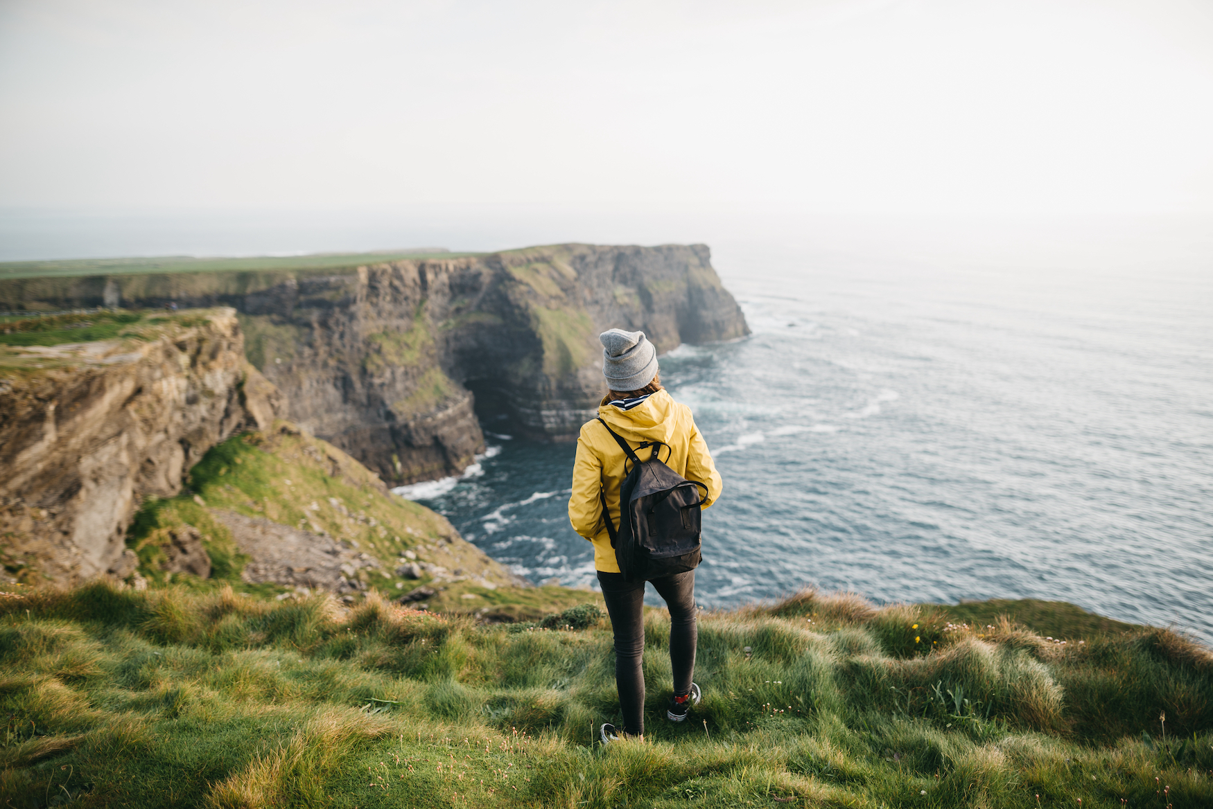 Wanderin in gelber Regenjacke steht auf den Cliffs of Moher