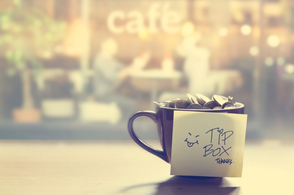 Tasse mit Trinkgeld-Münzen und einem Zettel mit der Aufschrift "Tip Box"