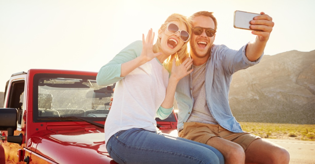 Paar auf Motorhaube eines Auto sitzend ein Foto machend