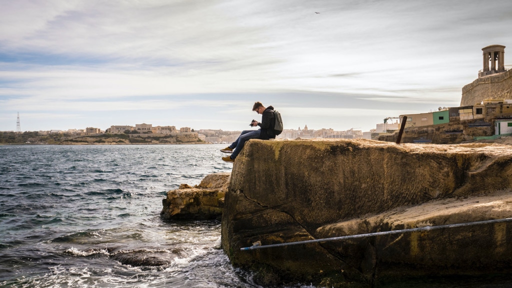 Mann mit einer Kamera sitzt auf einem Felsen am Meer in valletta