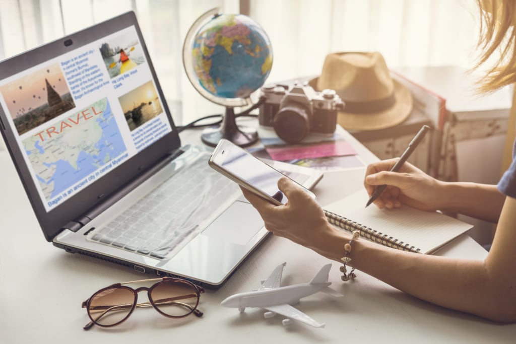 Frau plant ihren Urlaub am Laptop mit Weltkugel, Sonnenbrille, Sonnenhut am