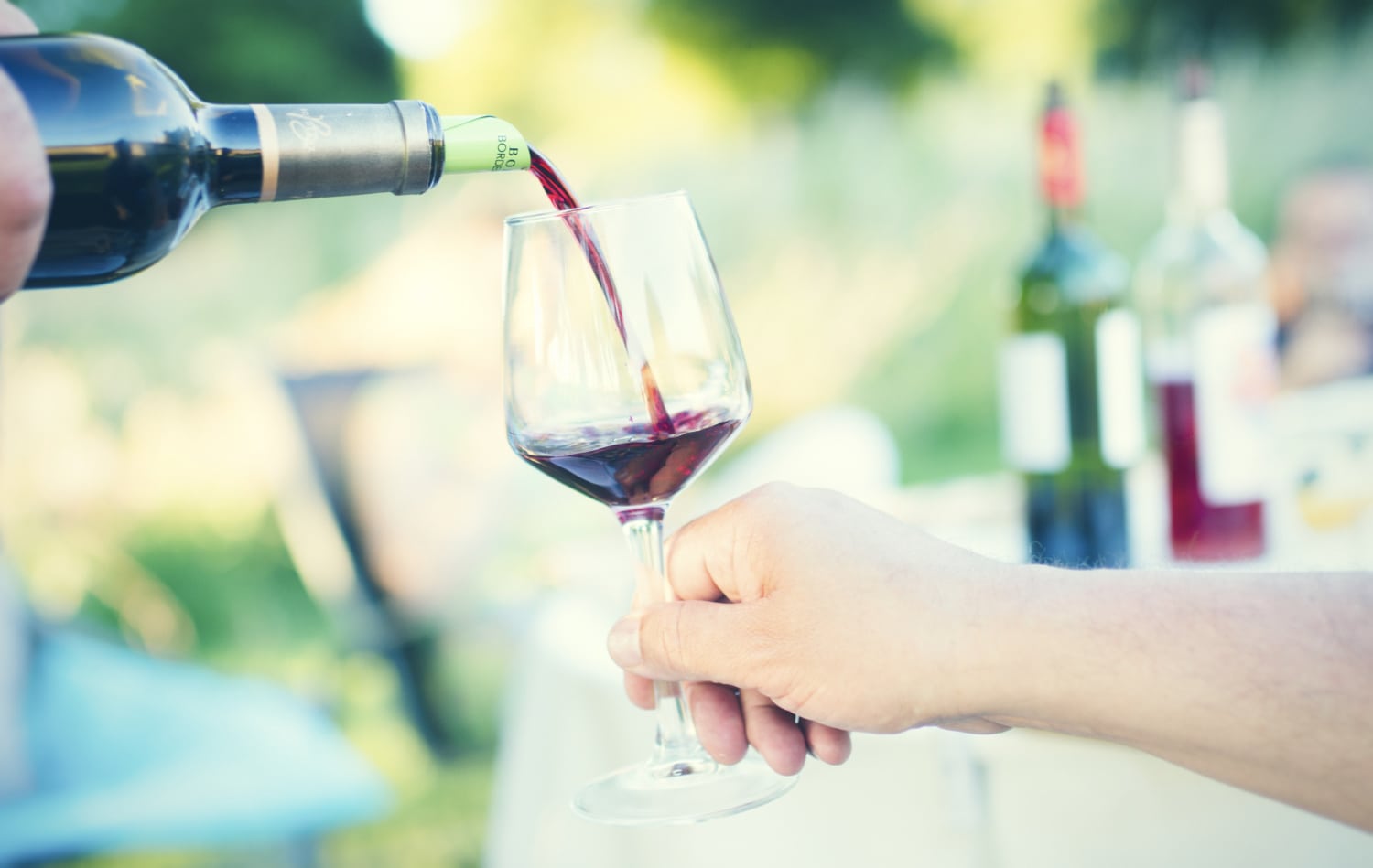 Frauenhand mit Weinglas, dass gerade mit Rotwein gefüllt wird.