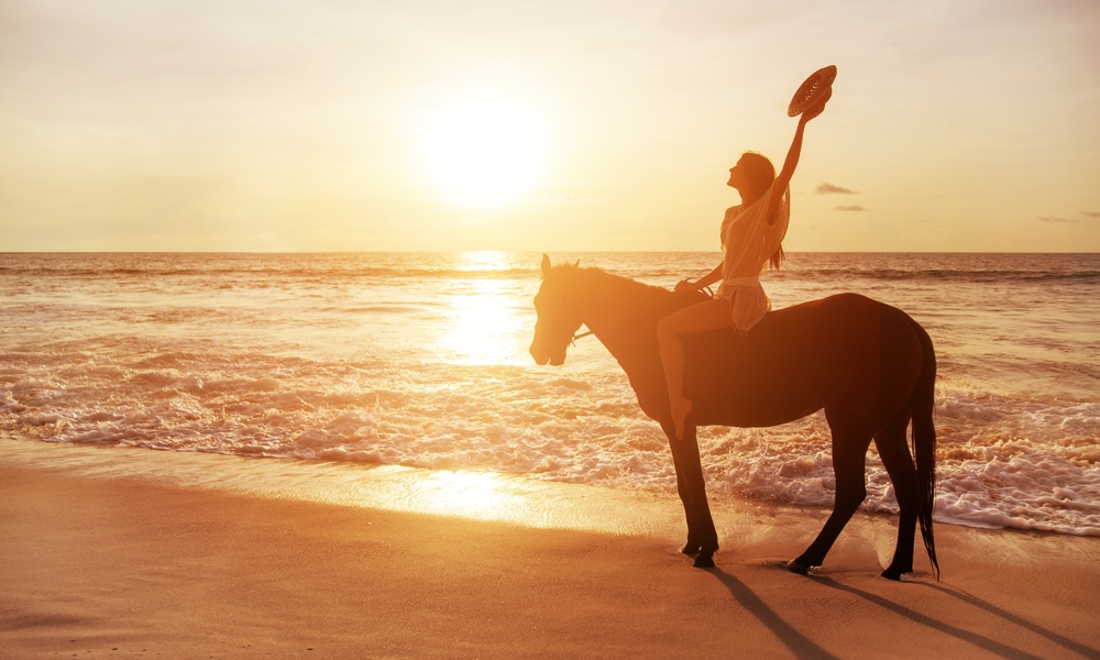 Frau reitet auf Pferd am Strand