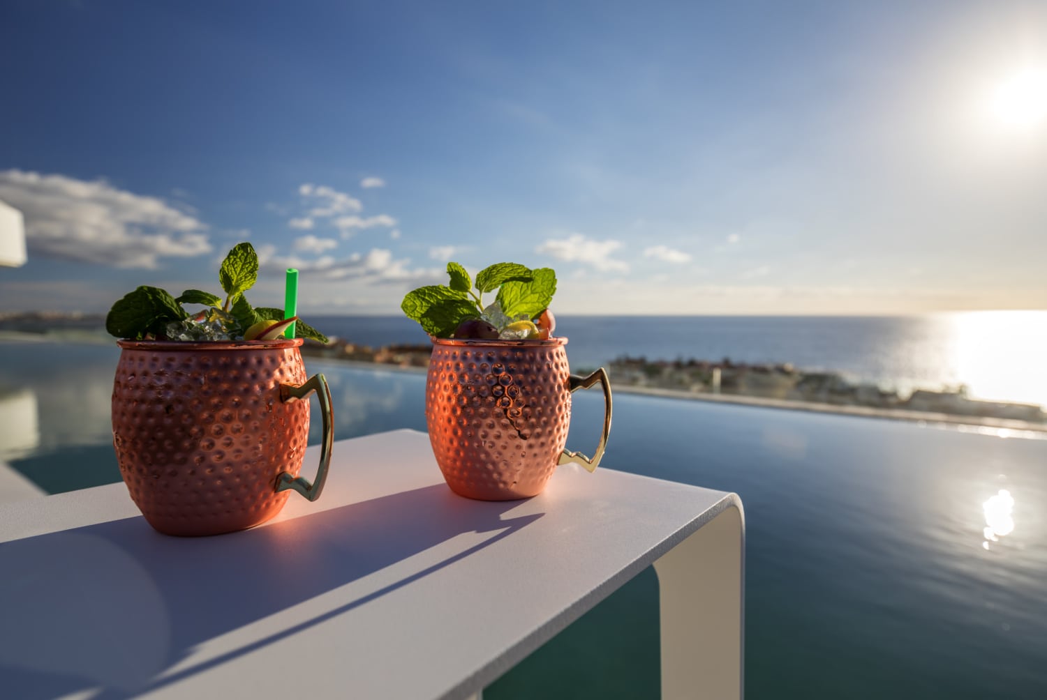Zwei Cocktails vor Pool mit Meerblick.