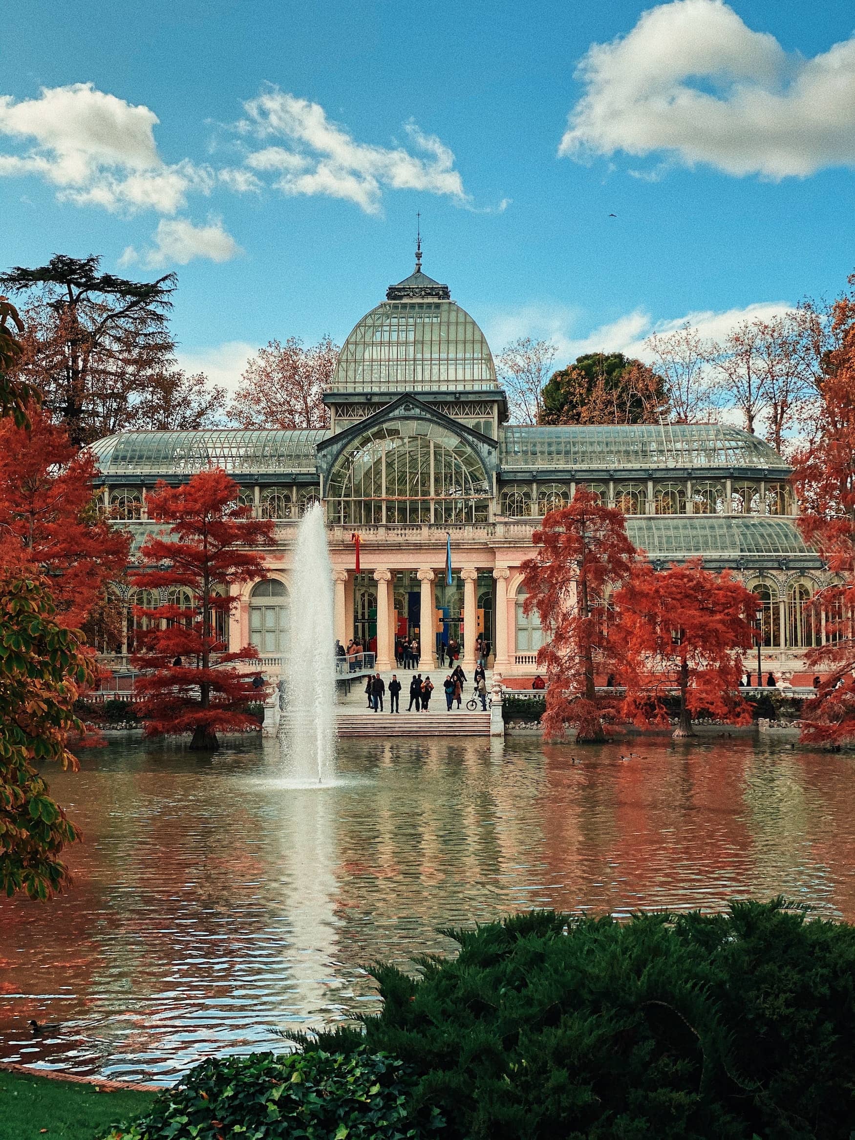 Rotes Laub hängt an den Bäumen vor dem Gewächshaus im Retiro Park in Madrid