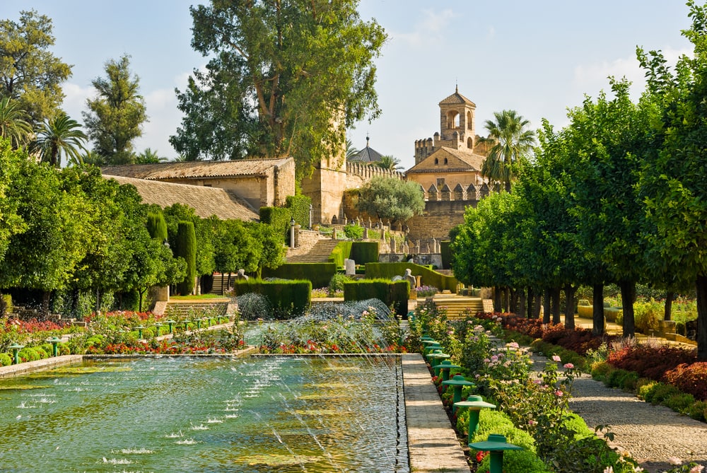 Grüner Garten mit altem Palast im Hintergrund und vielen Blumen und Brunnen.