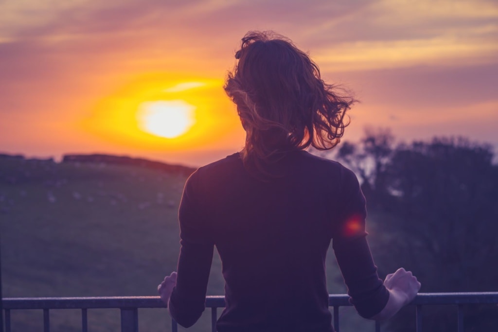 Frau auf Balkon stehend, blickt in Sonne