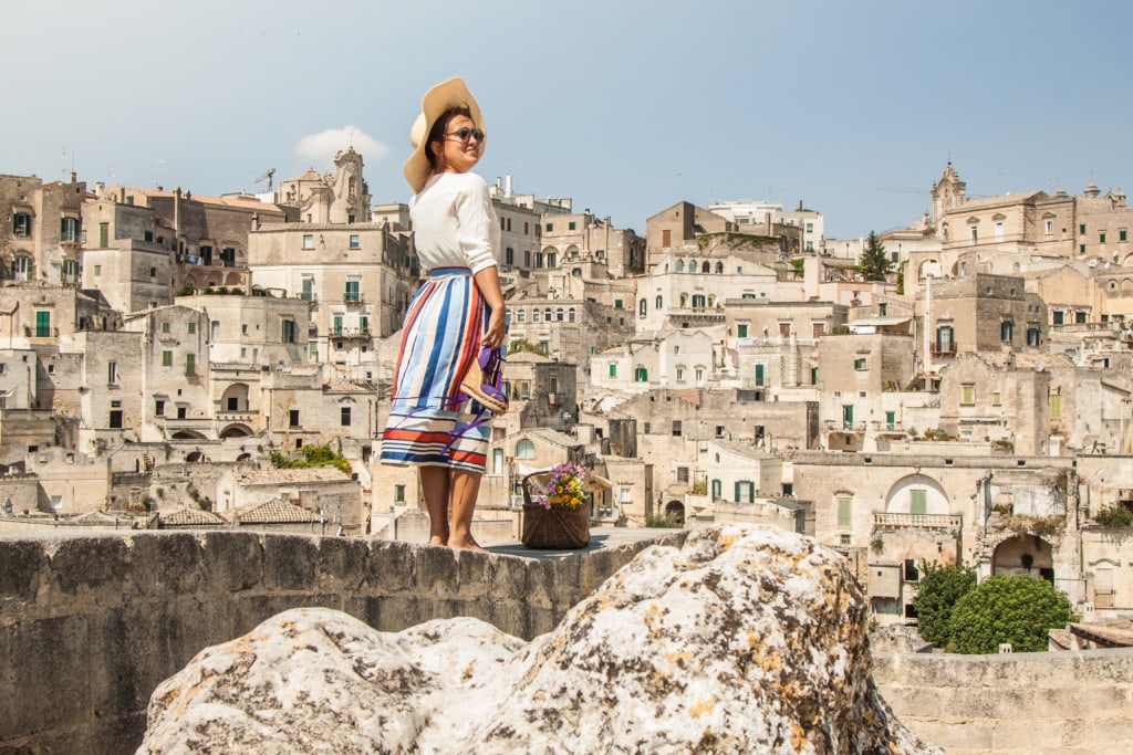 Frau mit Sonnenhut und Brille steht fotogen auf Mauer, im Hintergrund die Altstadt von Materna