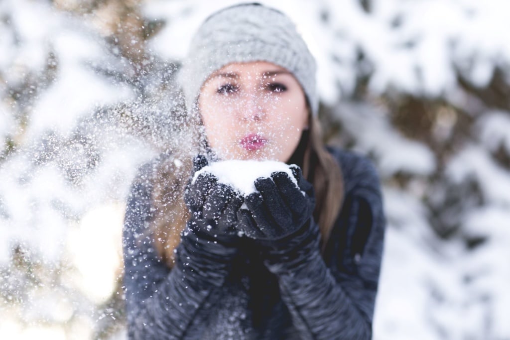 Frau in Winterlandschaft hält Schnee in der Hand, den sie wegpustet