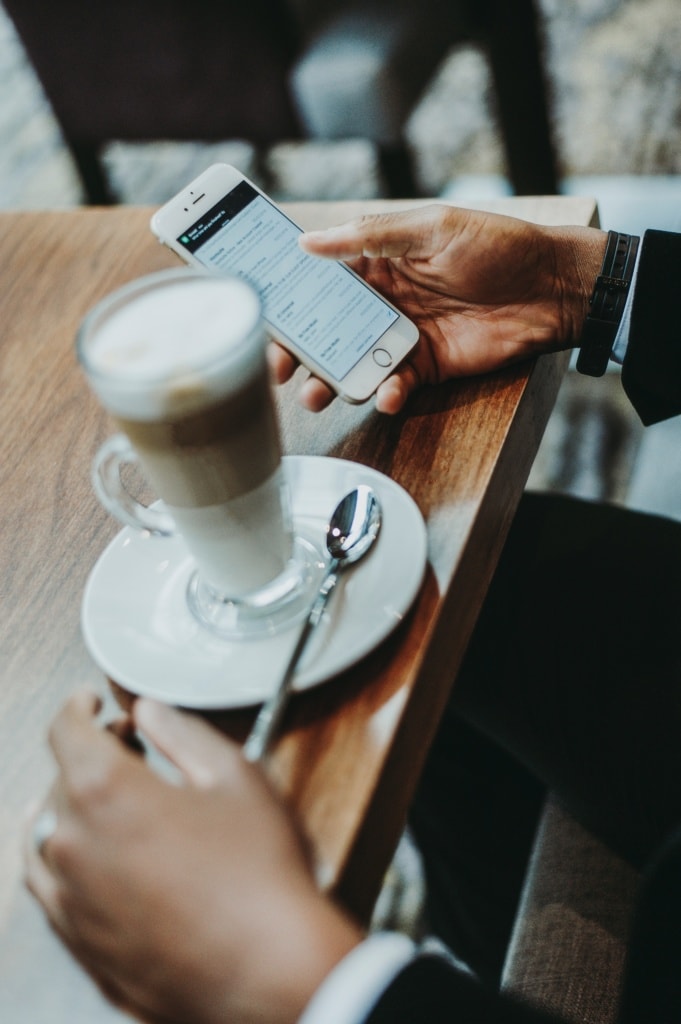 Person hält Handy in der Hand, auf Tisch ein Latte Macciato