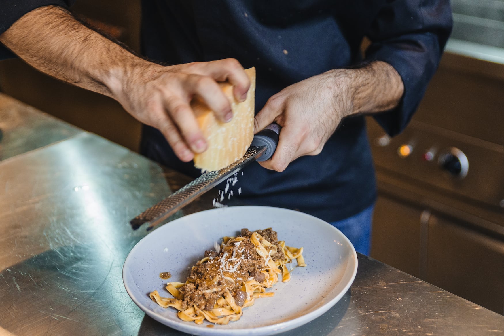Koch reibt Käse über Tagliatelle al Ragu