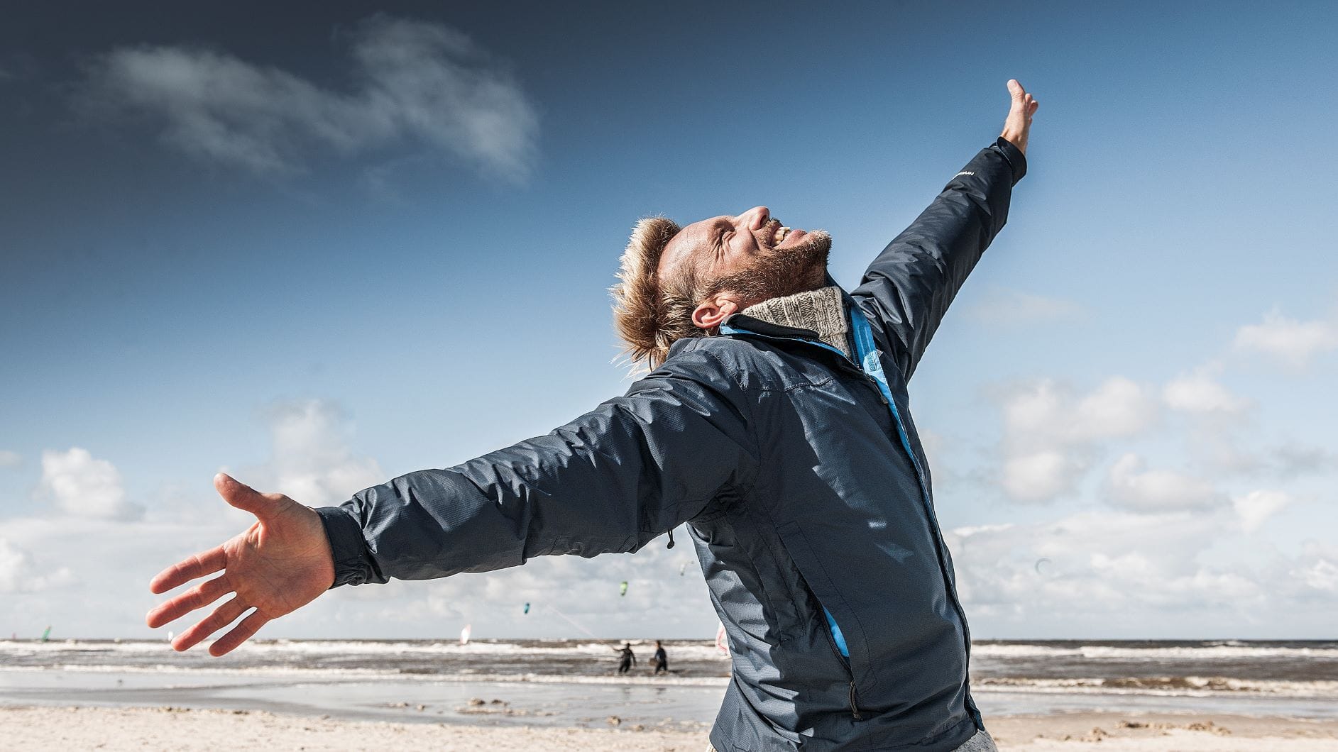 Mann breitet am Strand an der Nordsee die Arme aus