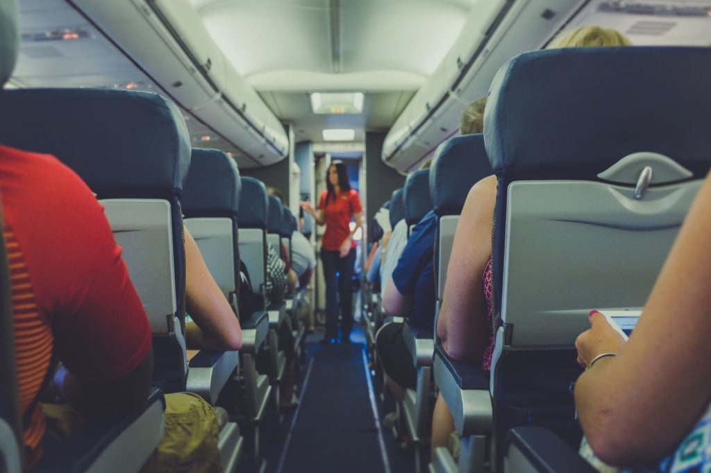 Gang im Flugzeug, Passagiere, im Hintergrund Flugbegleiterin