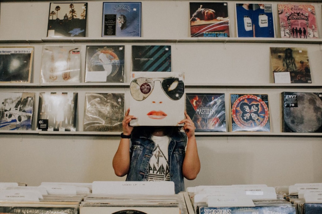 Frau hält sich im Schallplatten-Laden Cover vors Gesicht