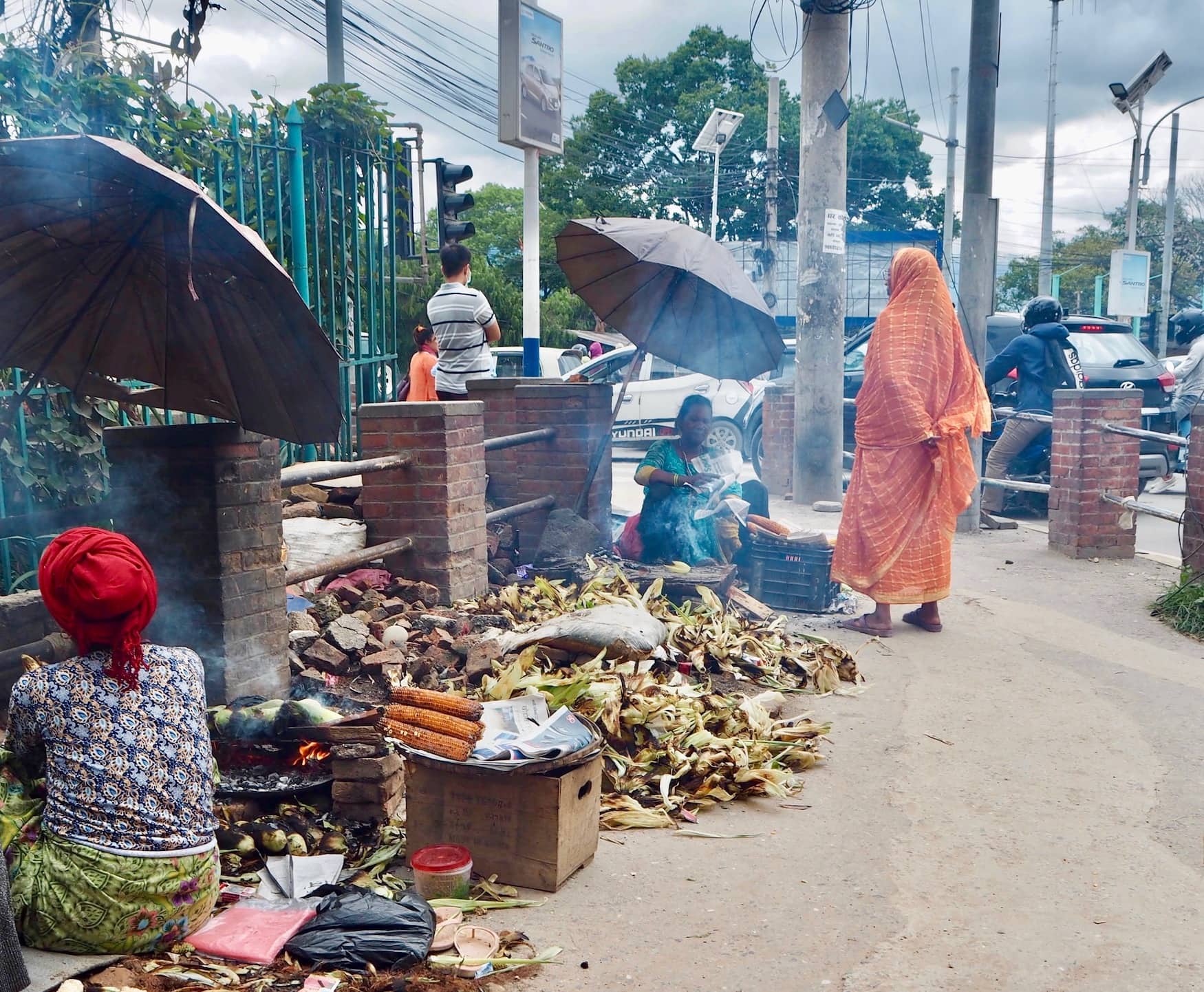 Frauen und Männer verkaufen gegrillte Maiskolben an Straßenrand in Kathmandu, Nepal