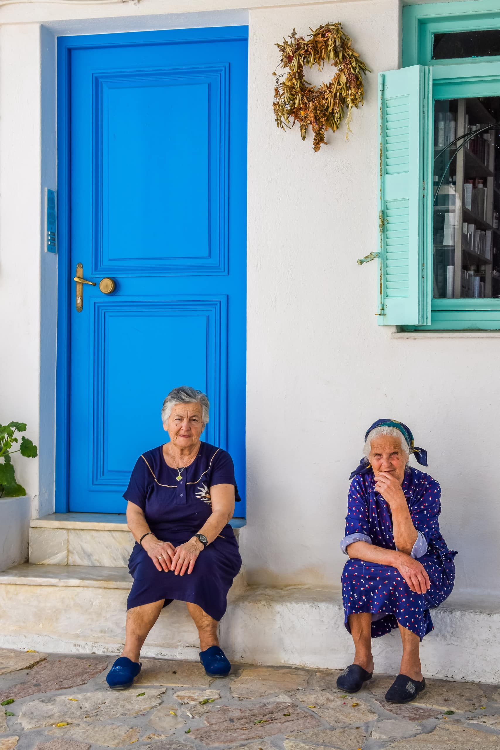 Zwei ältere Damen sitzen vor blauer Haustür auf einer griechischen Insel