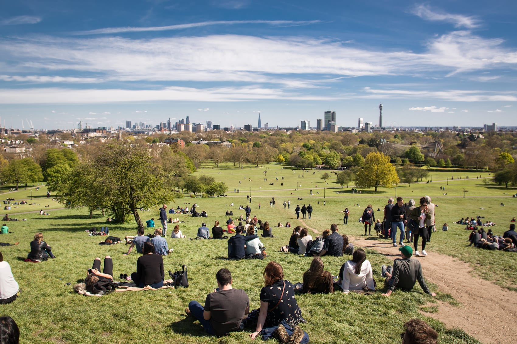 Von einem grünen Hügel, auf dem zahlreiche Menschen mit Picknickdecken sitzen, ist die Skyline von London sichtbar.