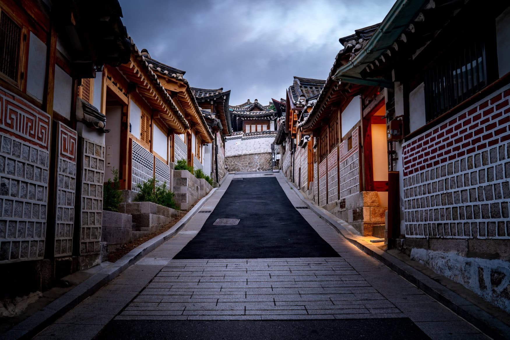 Blick in eine bergauf führende Straße im historischen Teil Bucheons in Südkorea. Der Himmel über den Dächern ist wolkenverhangen.