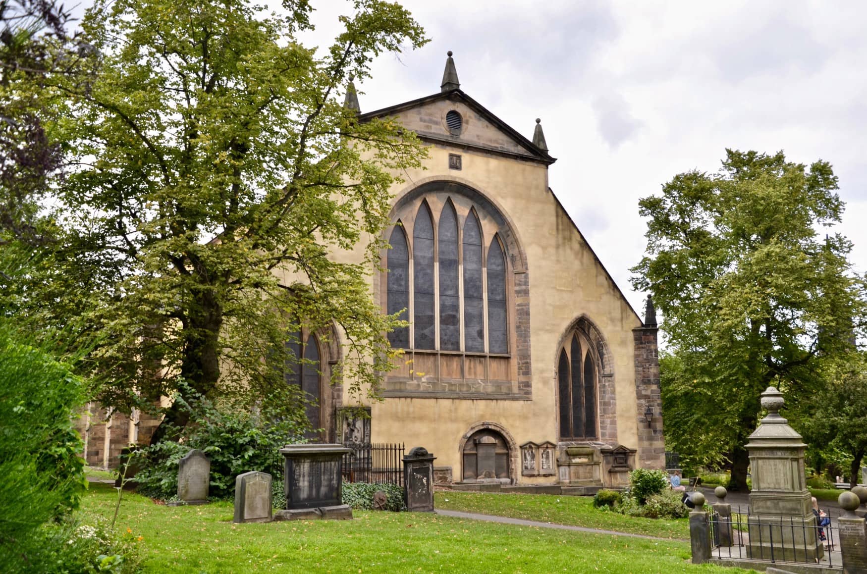 Ein mittelalterlicher Friedhof, dessen Grabsteine vor dem Chor eine gotischen Kirche stehen.