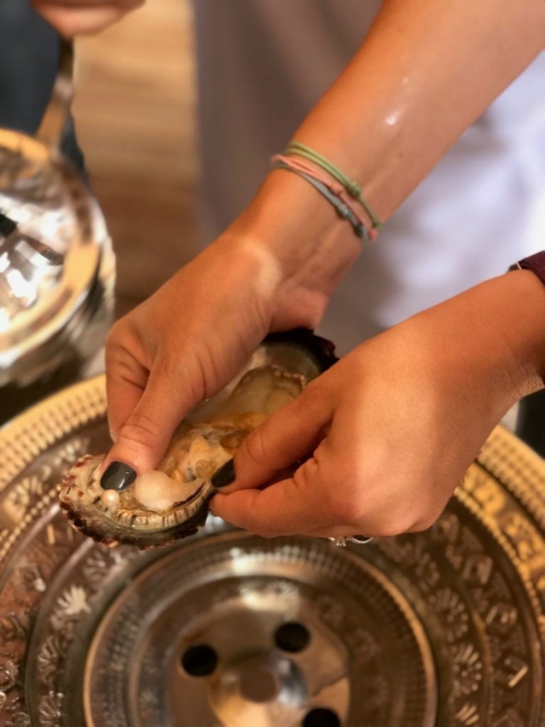 Frau hält Muschel mit Perle in der Hand