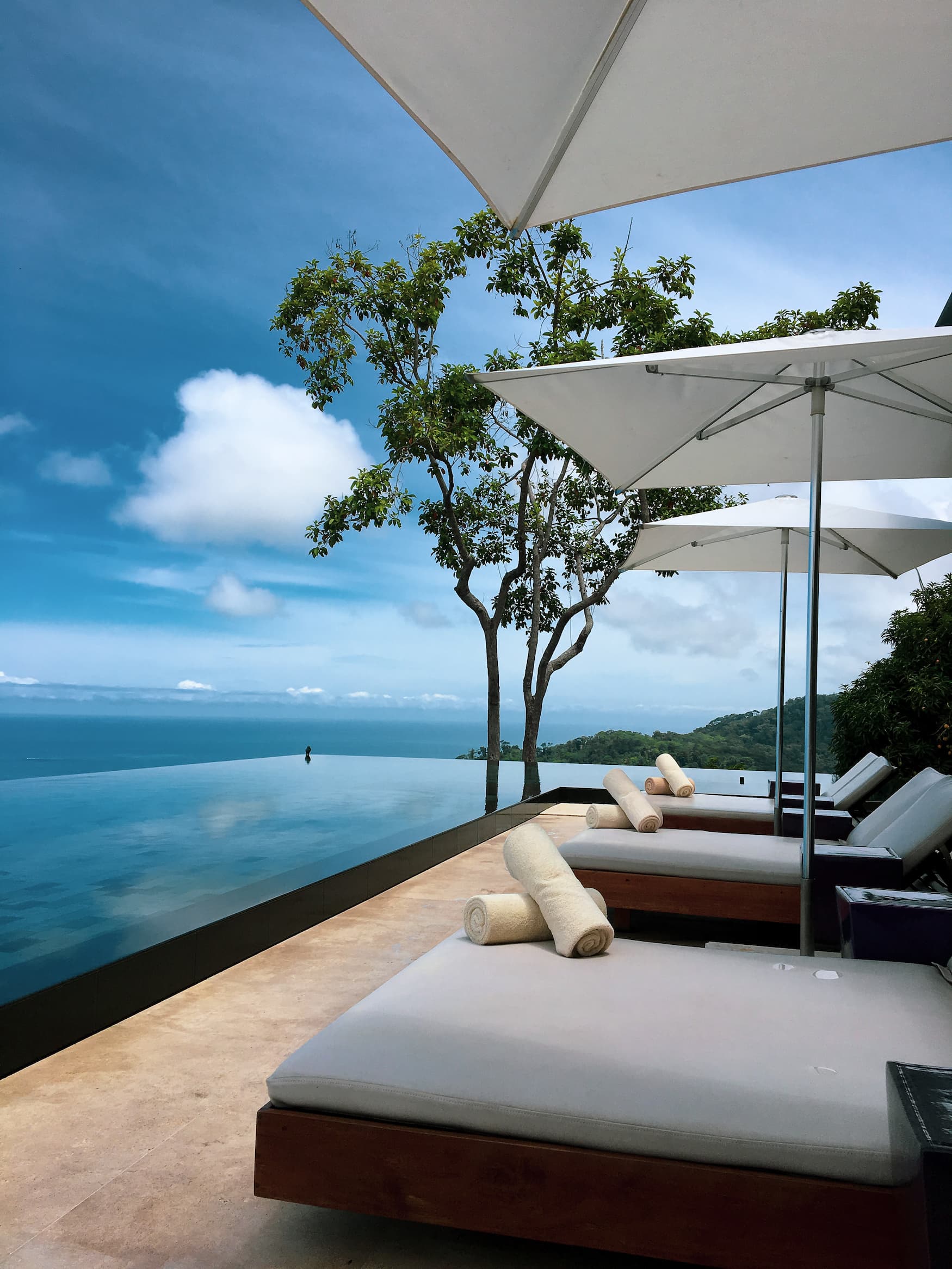 Liegen stehen nebem dem sich im Himmel spiegelnden Infinity-Pool mit Blick auf den Ozean