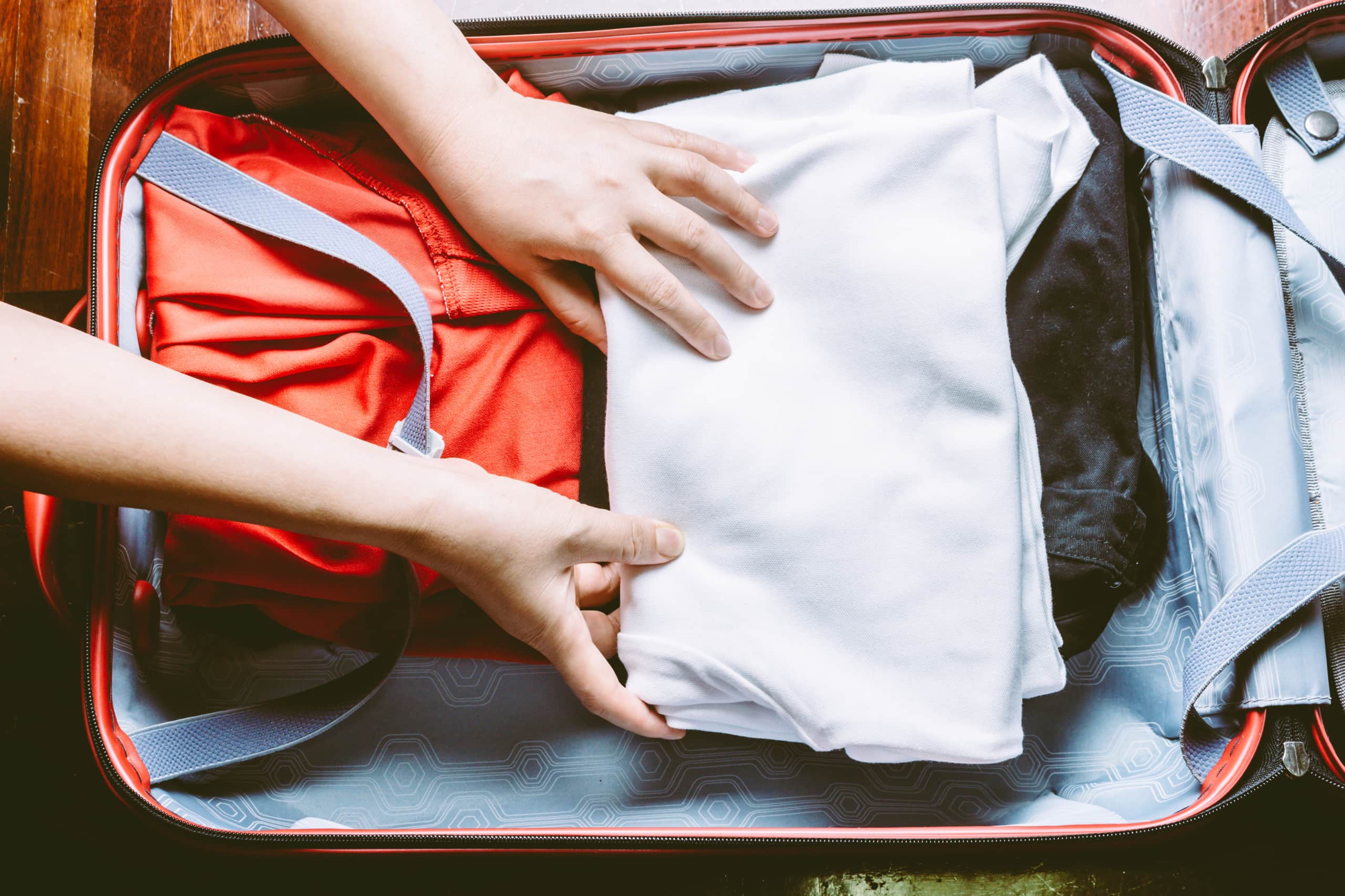 Frauenhände falten weißes Tshirt in gepacktem Koffer