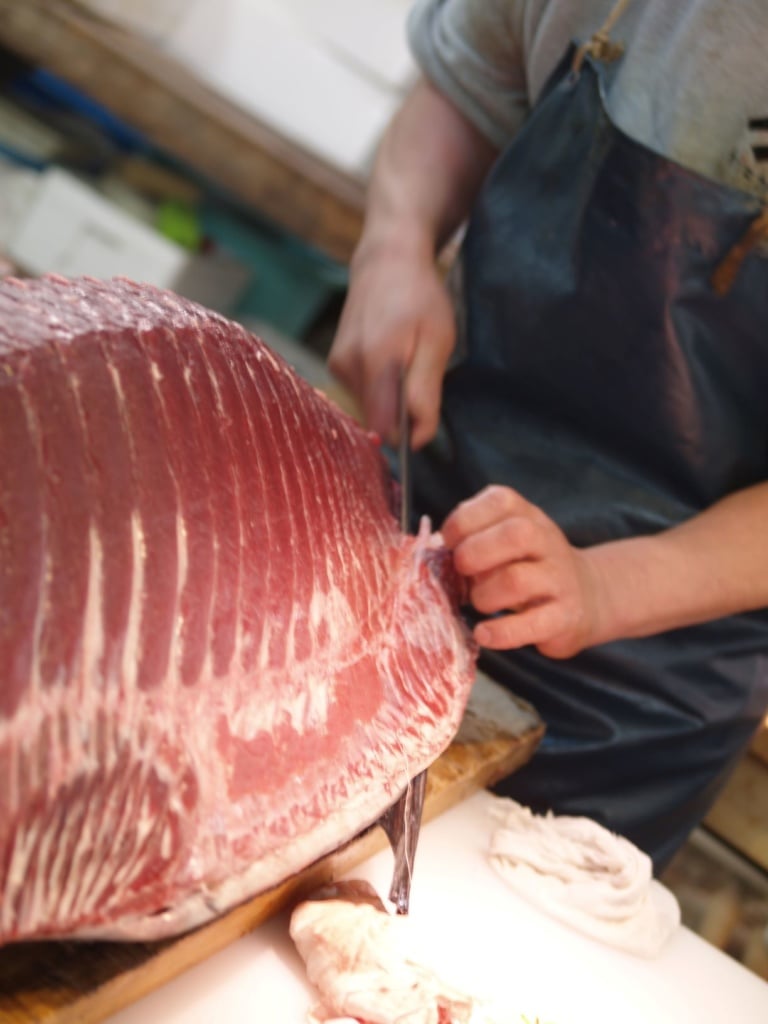 Mann schneidet großes Stück Fisch auf dem Fischmarkt in Tokio
